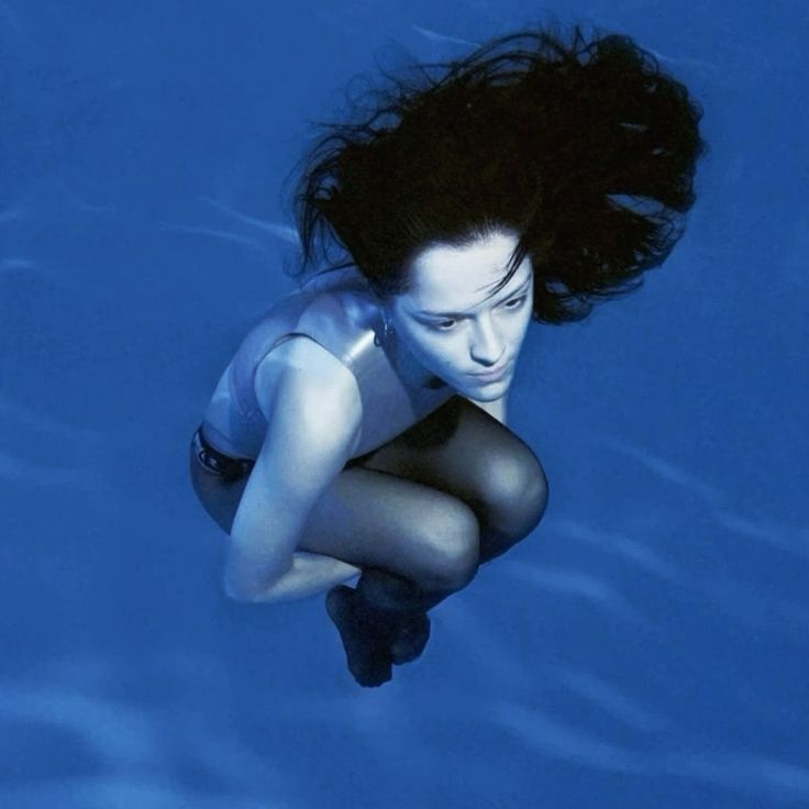 A photo of a girl floating underwater, hugging her knees.